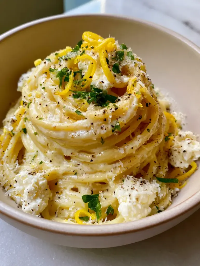 Elegantes Spaghetti-Nest in einer beigen Schüssel mit Zitronenzesten und Parmesan-Schnee. (zitronen-ricotta-pasta)